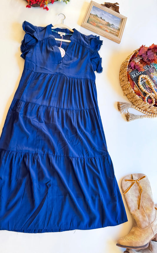 Navy tiered midi dress with flutter sleeves and pom pom trim, flat lay